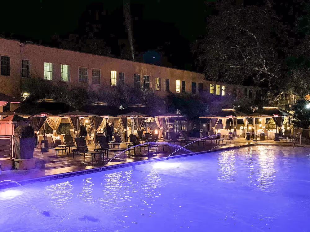 A pool with a fountain and chairs at nightDescription automatically generated