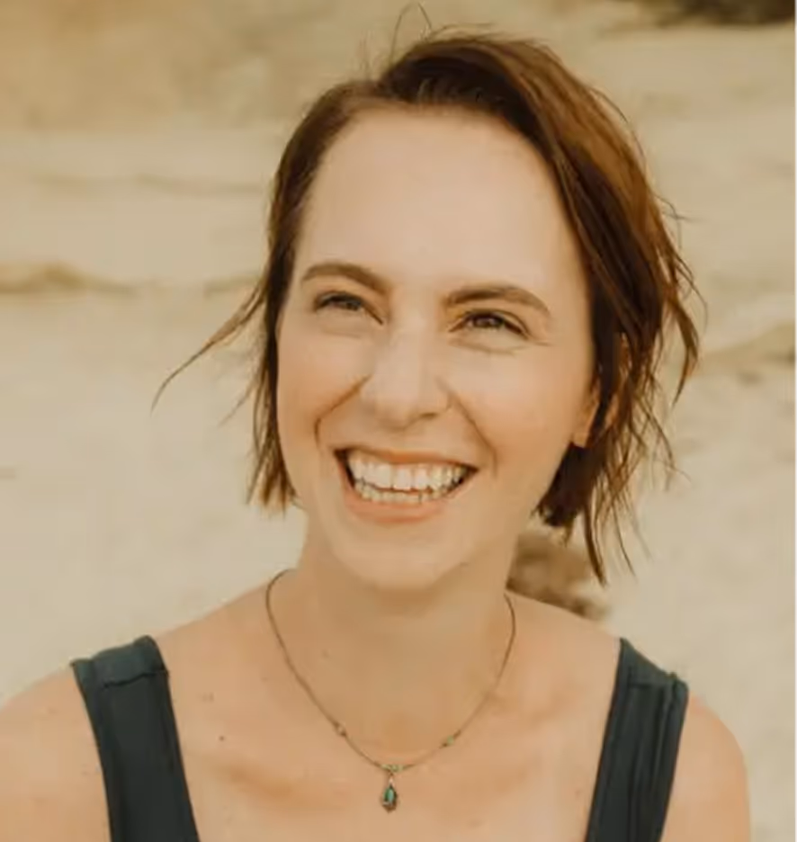 Smiling woman with short brown hair wearing a dark sleeveless top and a necklace with a green pendant.