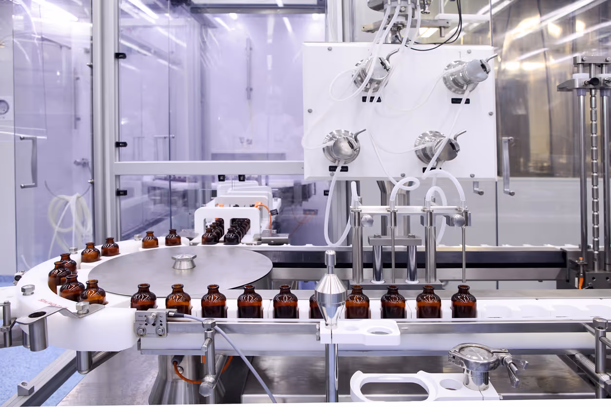 Automated pharmaceutical production line with brown glass bottles moving on conveyor belts for filling and packaging.