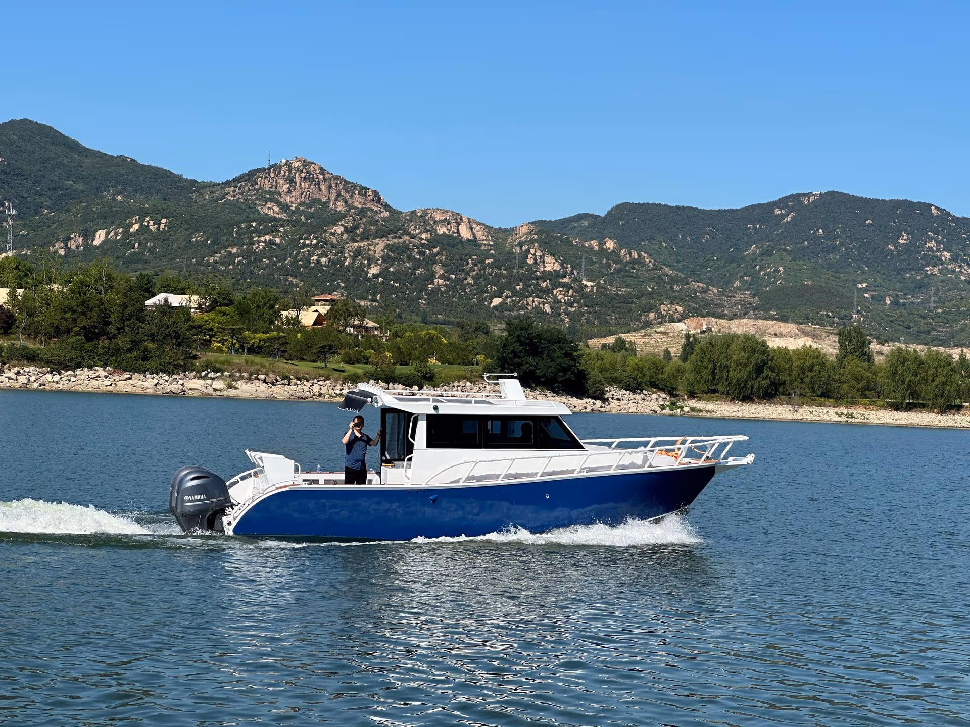 Blue and white motorboat cruising on lake with mountainous landscape in the background.