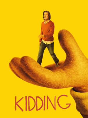 A man in an orange sweater walking on an oversized golden hand against a yellow background with the word 'KIDDING' below.
