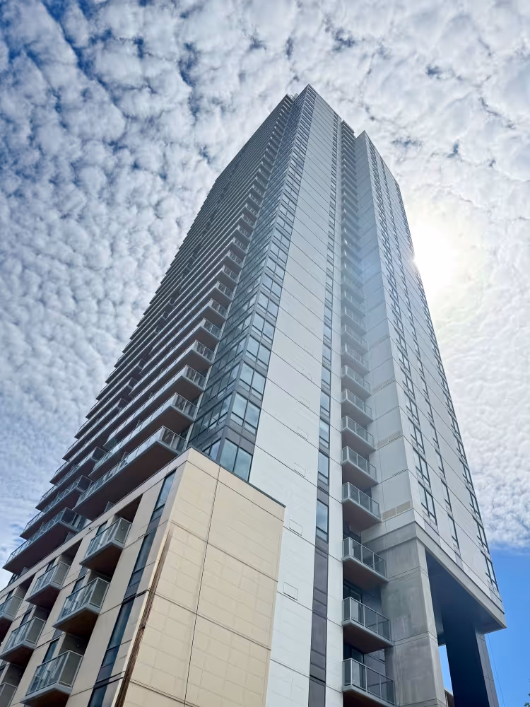 Low-angle view of a tall modern residential building with balconies against a partly cloudy sky.