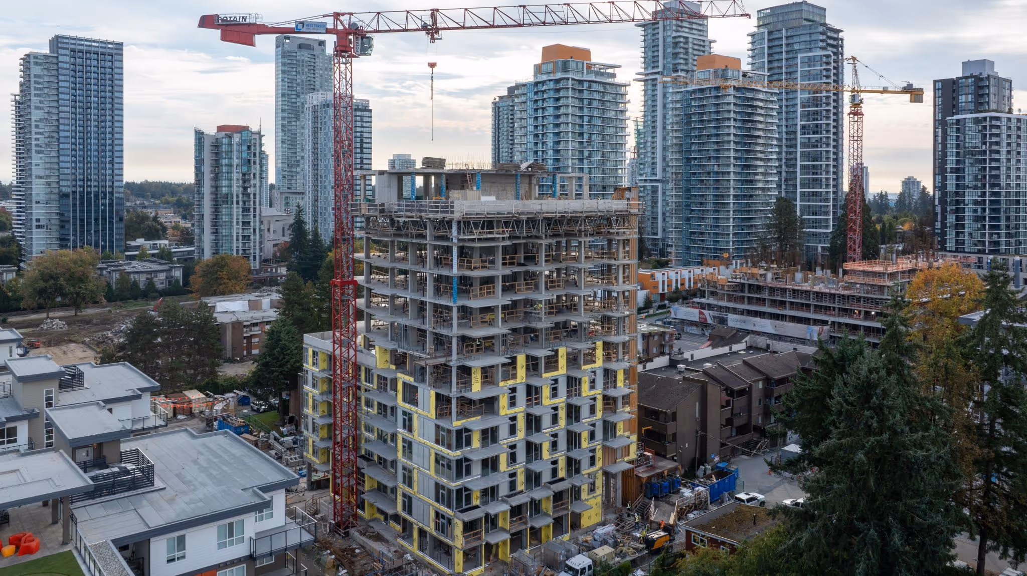 High-rise building under construction with cranes amidst completed residential towers in an urban area.