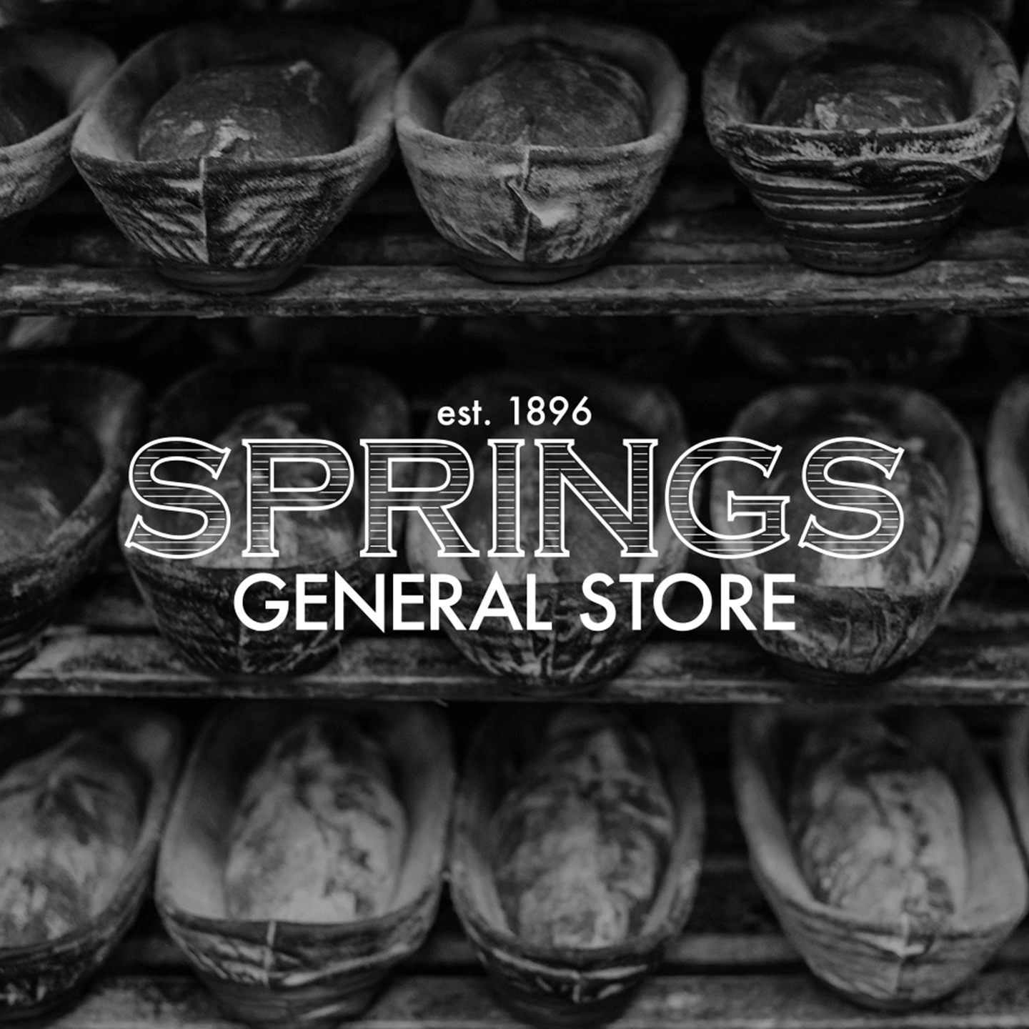 Loaves of bread in proofing baskets on shelves with overlay text est. 1896 SPRINGS GENERAL STORE.