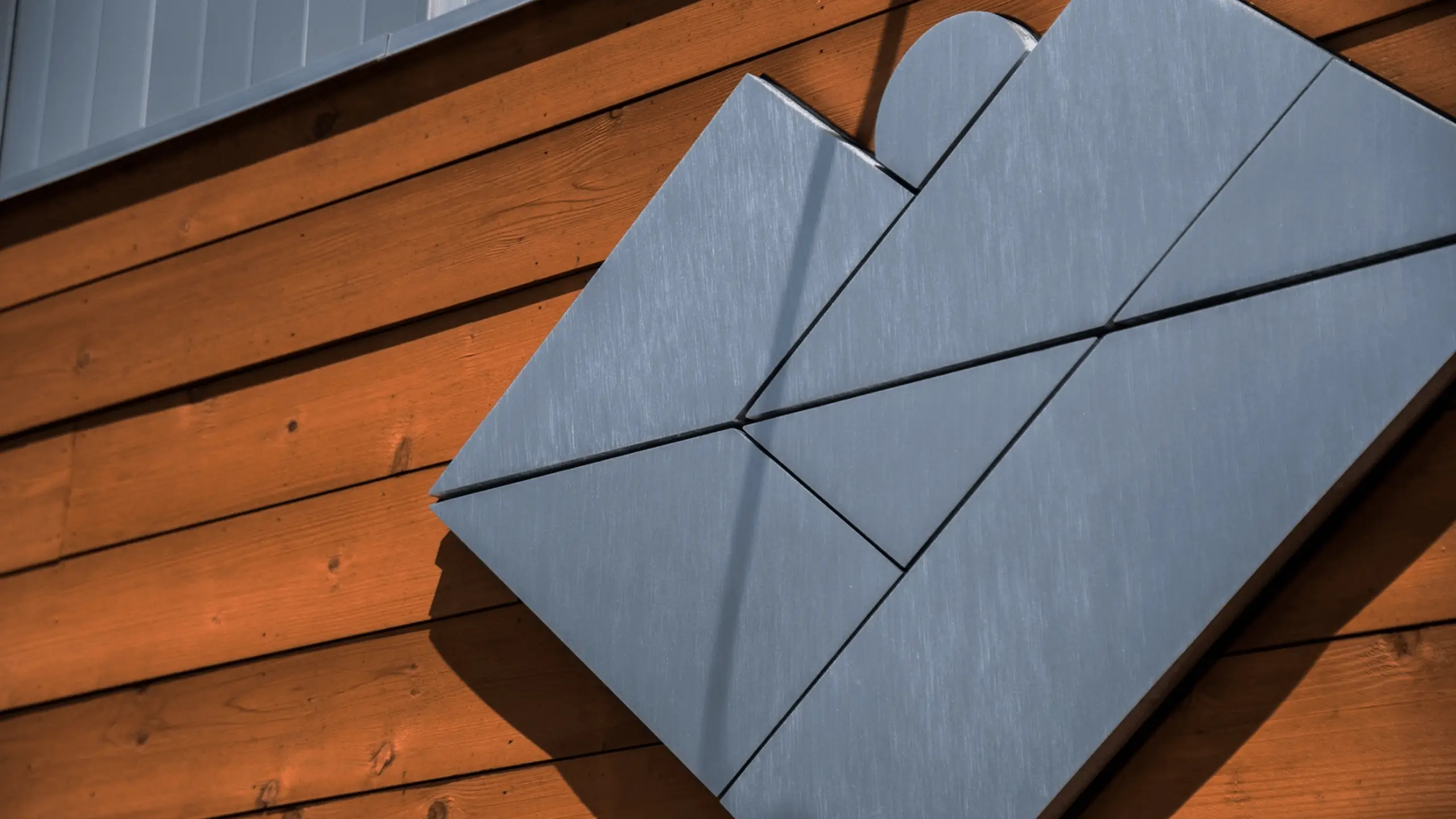 Modern geometric metal sign mounted on a wooden slat wall with warm lighting.