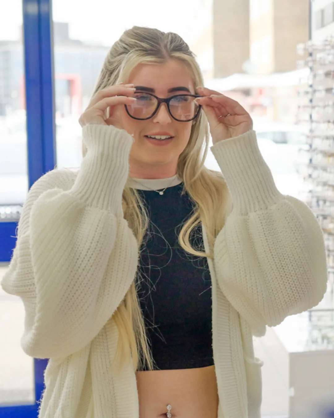 Woman trying on prescription glasses inside a modern opticians store