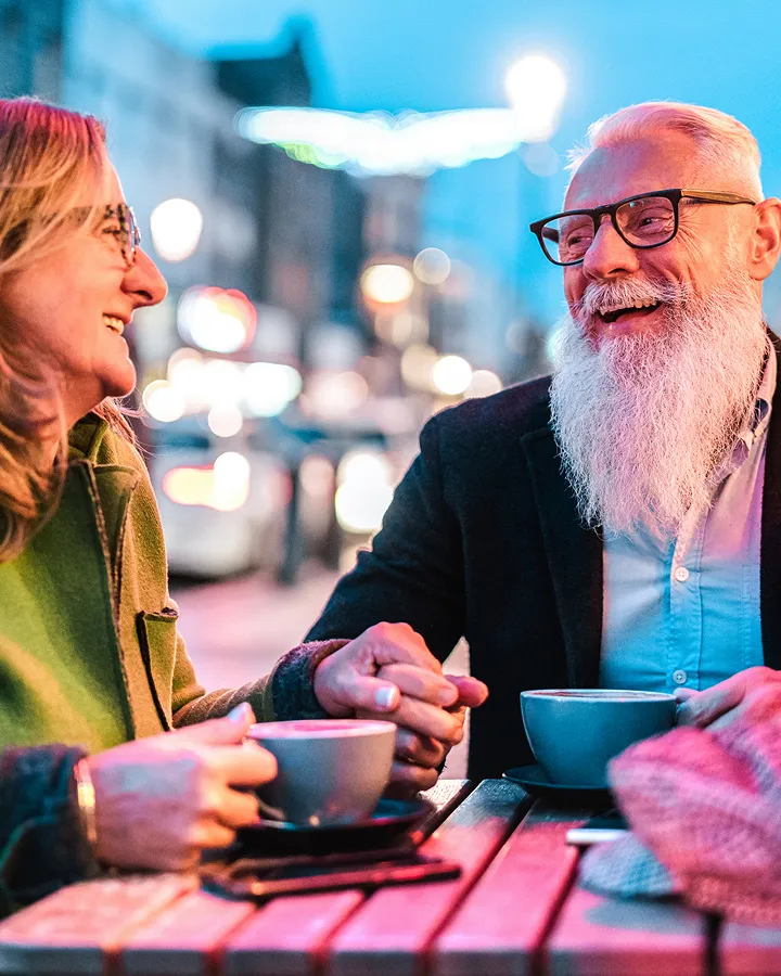 Happy mature couple wearing glasses enjoying conversation at outdoor cafe after hearing test"