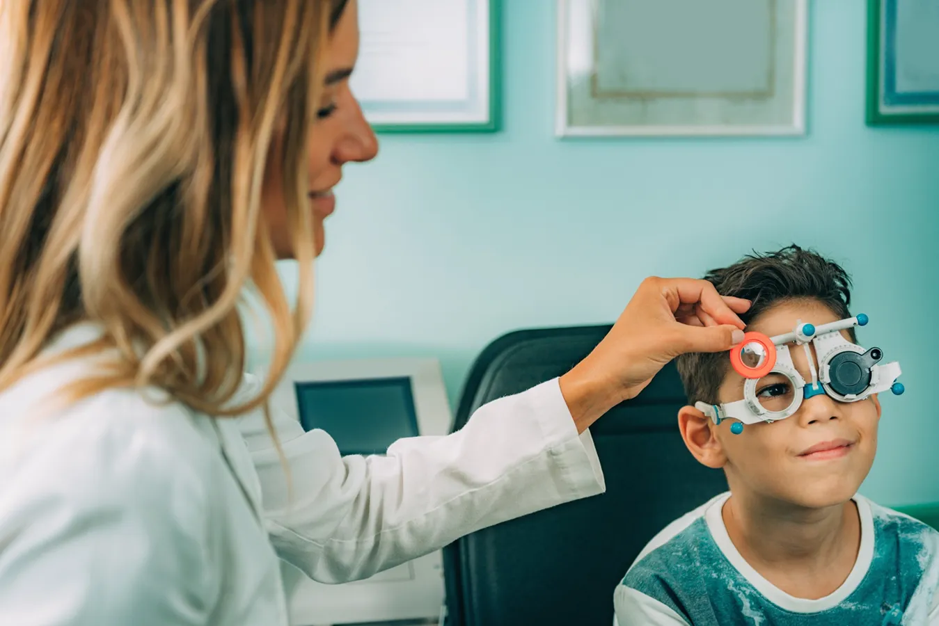 Optometrist performing pediatric eye examination on child using phoropter testing equipment
