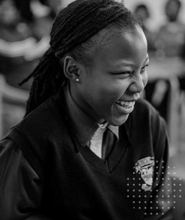 Black and white photo of a smiling young woman with dreadlocks wearing a sweater with a crest emblem.