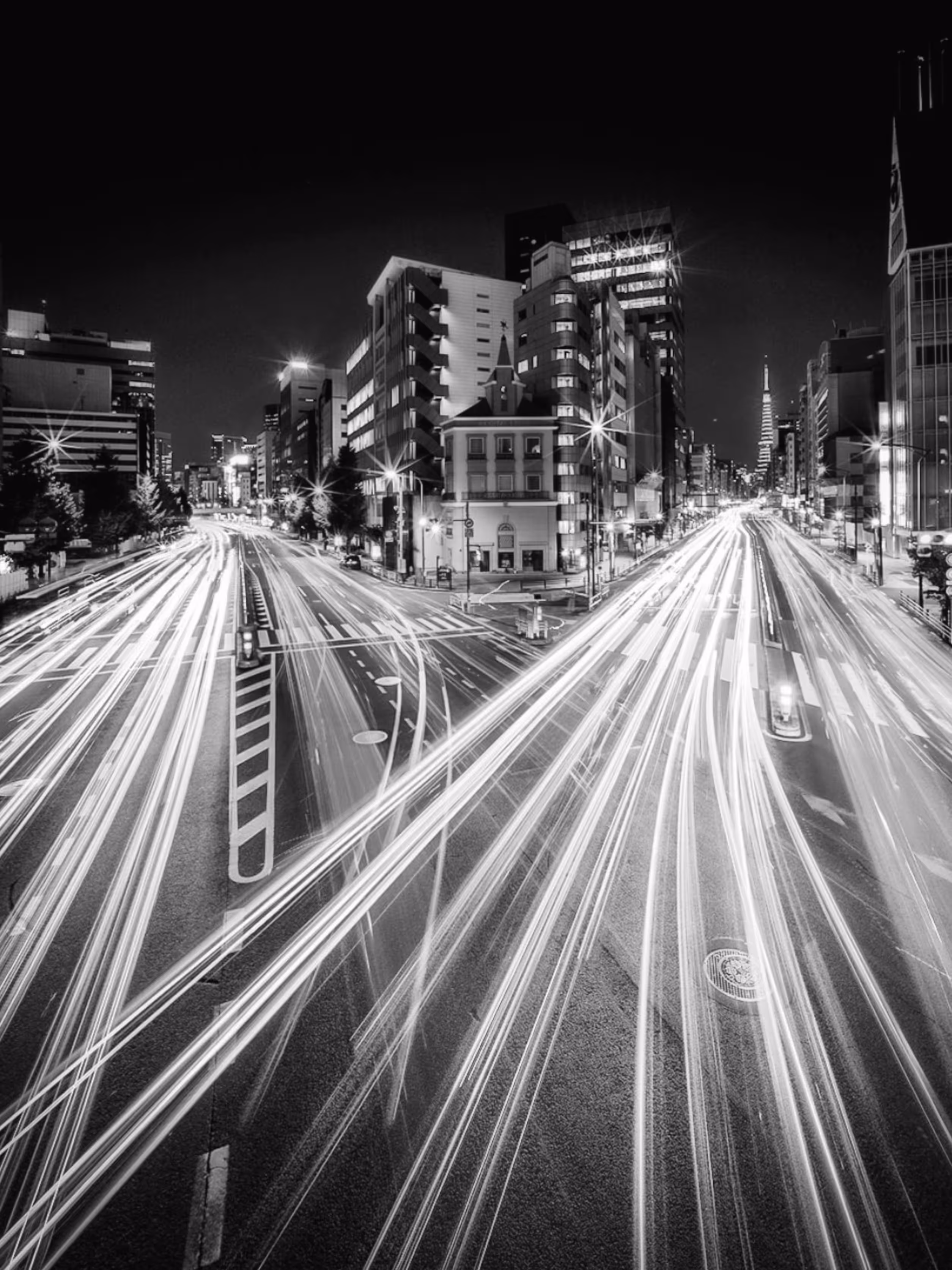 Lichtsporen van verkeer op een drukke stedelijke snelweg met hoogbouw aan beide zijden bij nacht.
