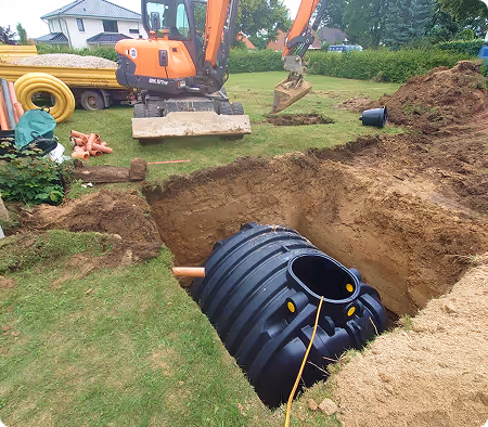 Bagger gräbt einen großen Graben im Garten, in dem ein schwarzer Kunststofftank installiert wird.