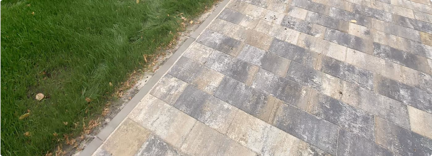 Gepflasterter Weg neben einer grasbewachsenen Grünfläche mit einigen verstreuten Herbstblättern.