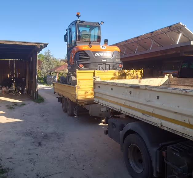 Kleiner Doosan-Bagger auf gelbem LKW-Anhänger auf einem Hof bei klarem Himmel.