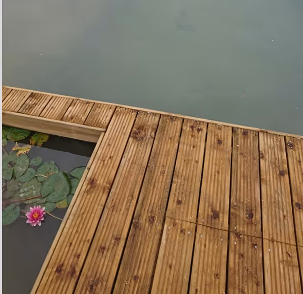 Holzsteg über ruhigem Wasser mit Seerose und grünen Blättern am Rand.
