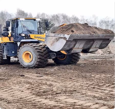 Gelber und schwarzer Radlader mit voller Schaufel Erde auf einer Baustelle.