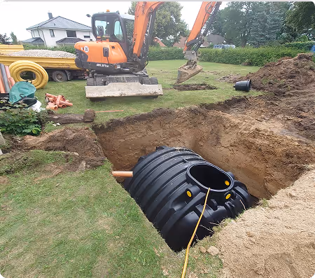 Schwarzfarbener Wasserspeichertank, der in eine gegrabene Bodenvertiefung auf einem Rasen gelegt wird, mit einem orangefarbenen Bagger und Baumaterialien im Hintergrund.