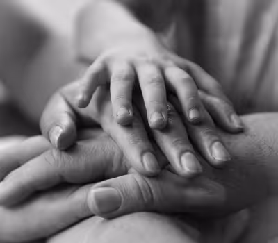Close-up black and white photo of adult and child hands stacked in a gesture of support and care.