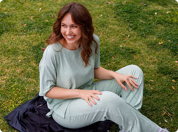 Smiling woman in light green outfit sitting on grass with a dark cloth beneath her.
