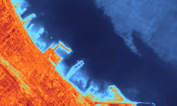 Thermal aerial view of a coastal urban area with buildings and docks showing heat signatures in warm colors against cooler blue water.