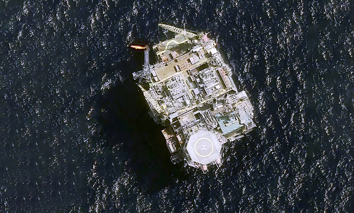Aerial view of an offshore oil platform in the ocean with a helipad and burning flare.