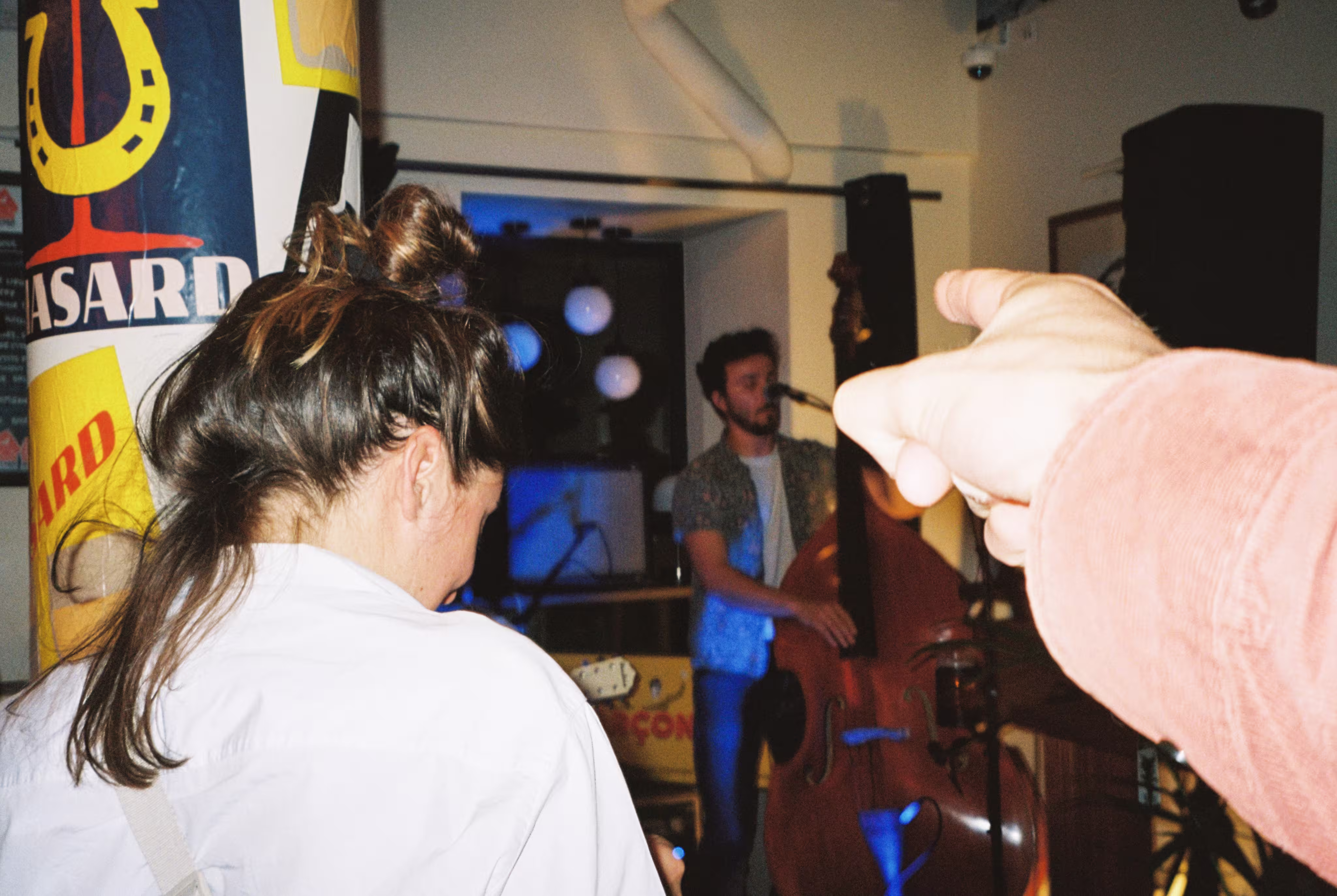 Une main pointant vers un musicien jouant de la contrebasse lors d'un concert en intérieur.