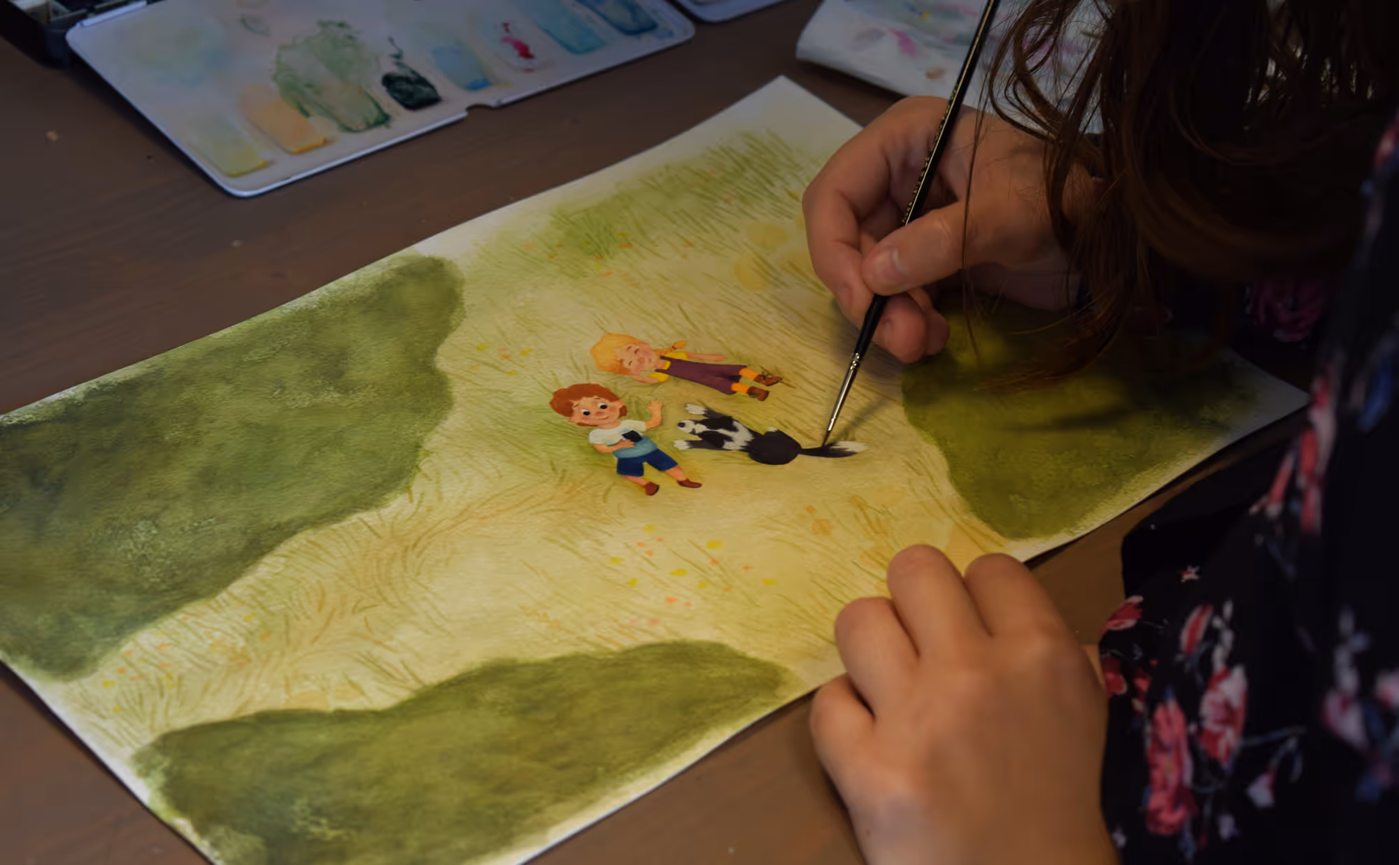 Calle schildert een illustratie van twee kinderen en een hond in een grasveld.