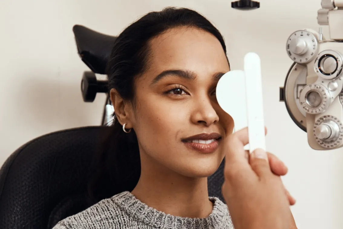 Woman having an eye exam covering one eye with an occluder at an optometrist's office.