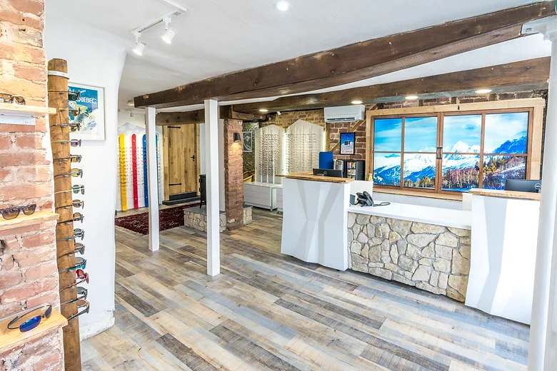 Bright eyewear store interior with wooden beams, stone and white counters, and sunglasses displayed on a wooden wall rack.