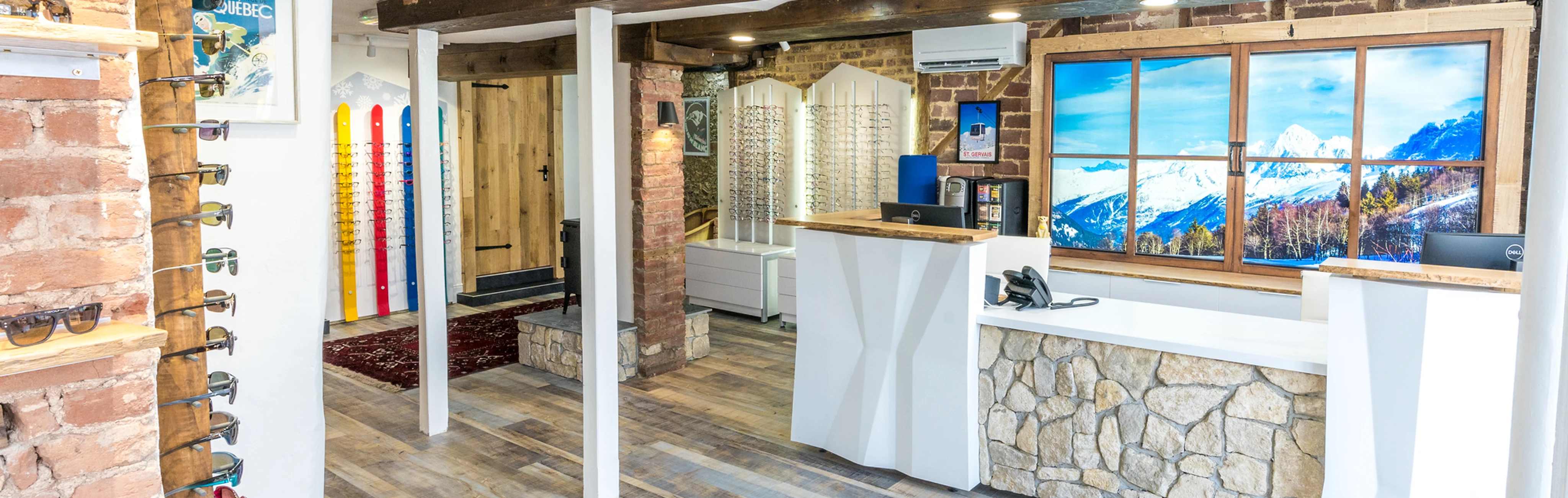 Bright interior of an eyewear store with wooden and stone accents, sunglasses on display, and a large window featuring a snowy mountain landscape.