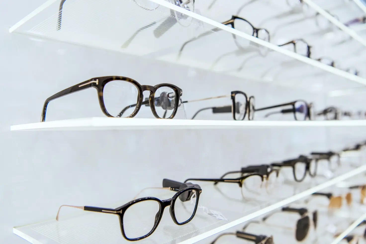 Rows of eyeglasses with various styles displayed on glass shelves in an optical store.