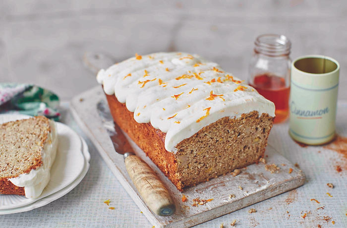 Avocado and banana bread loaf topped with white frosting and orange zest on a wooden board.
