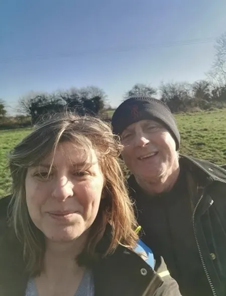 Selfie of two people outdoors in winter clothing with a field and bare trees in the background.