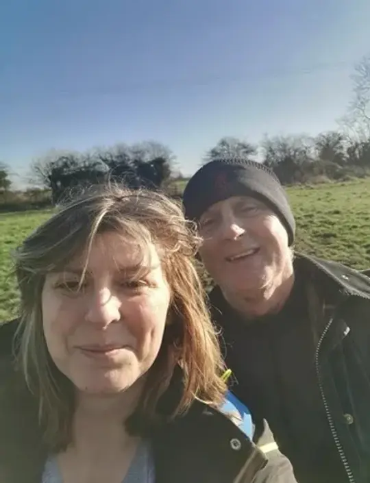 Selfie of two people outdoors in winter clothing with a field and bare trees in the background.