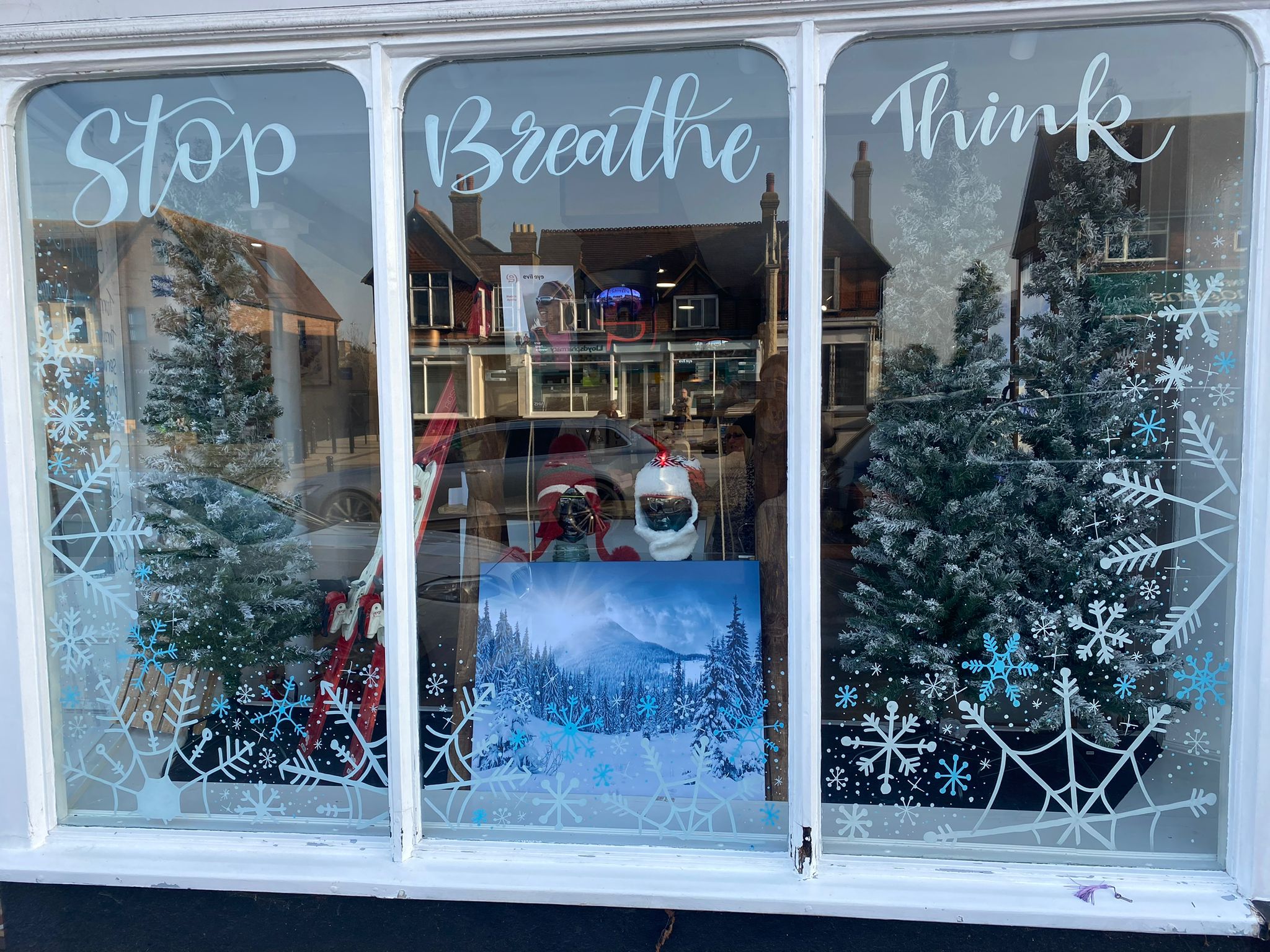 A calming winter window display featuring the words "Stop Breathe Think" across three panels, decorated with frosted Christmas trees, snowflake designs, and a winter mountain scene with Santa and elf figures.