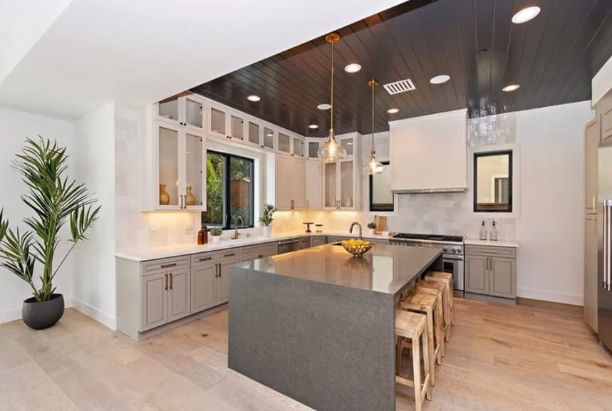 Maple Residence kitchen with waterfall island, two-tone cabinetry, dark ceiling detail, and views to the yard.