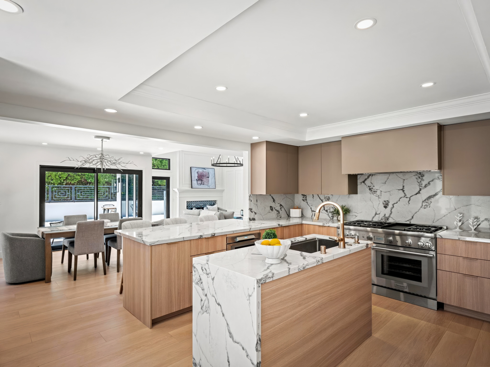 Whitewater Residence kitchen with marble waterfall island, warm wood accents, full-height stone backsplash, and pendant lighting.