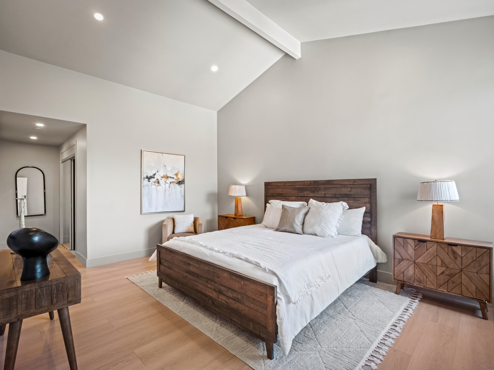Whitewater Residence bedroom with vaulted ceiling, warm wood floors, and soft coastal neutral styling.