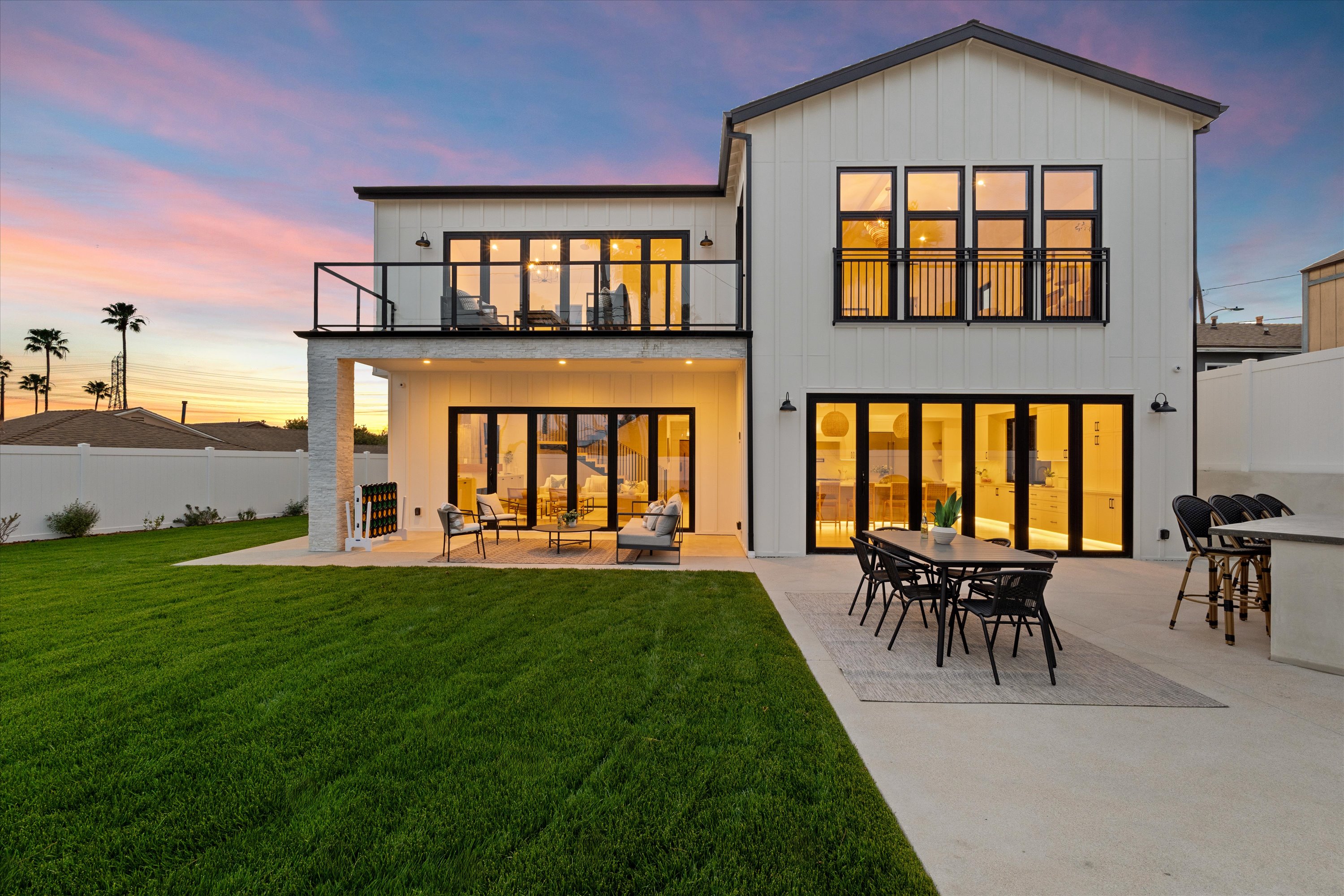 Modern two-story Cluster Residence with large glass doors, outdoor dining area, lounge seating, and green lawn at sunset.