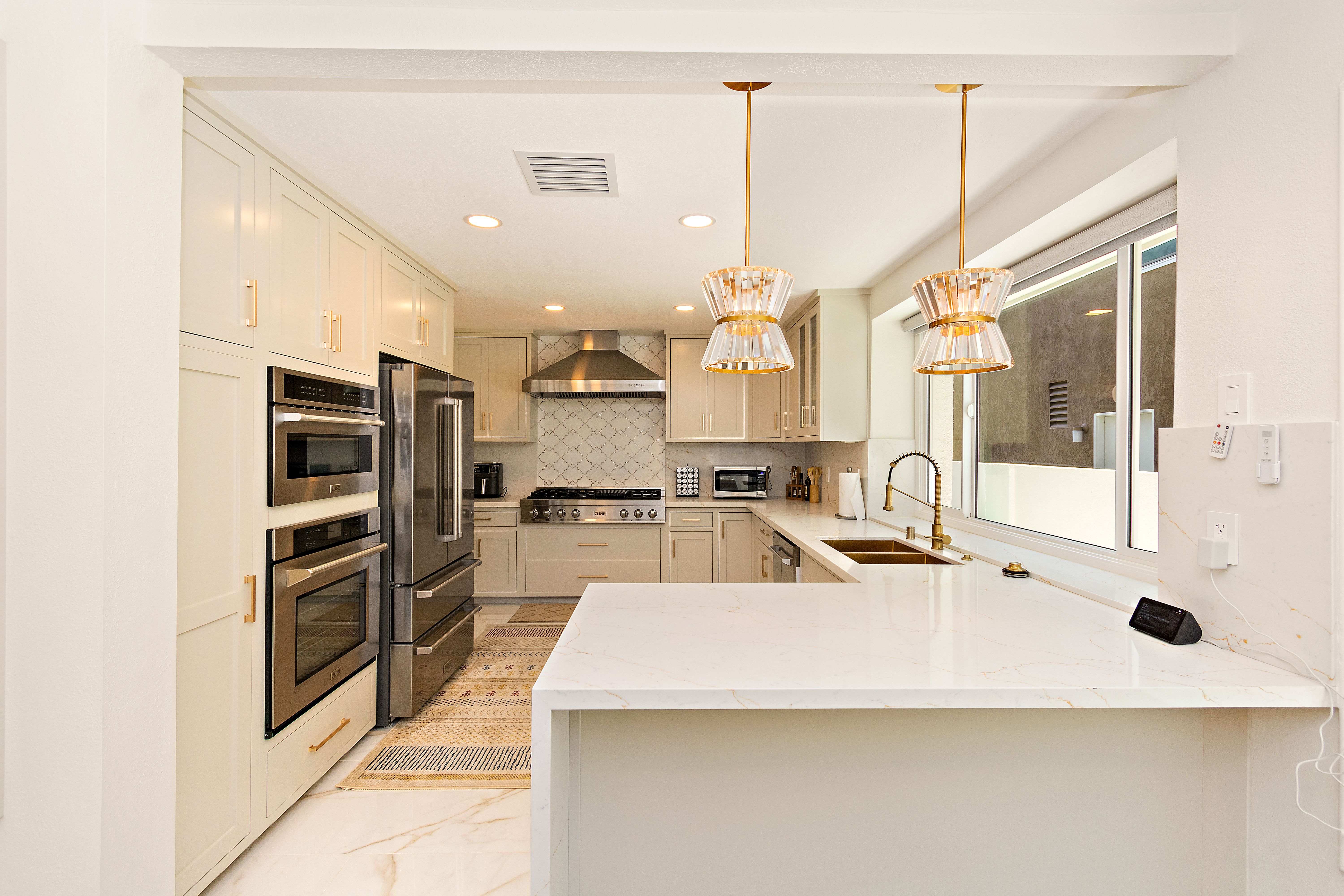 Rainstar Residence kitchen with soft-toned cabinetry, waterfall island, brass hardware, and statement pendant lights.