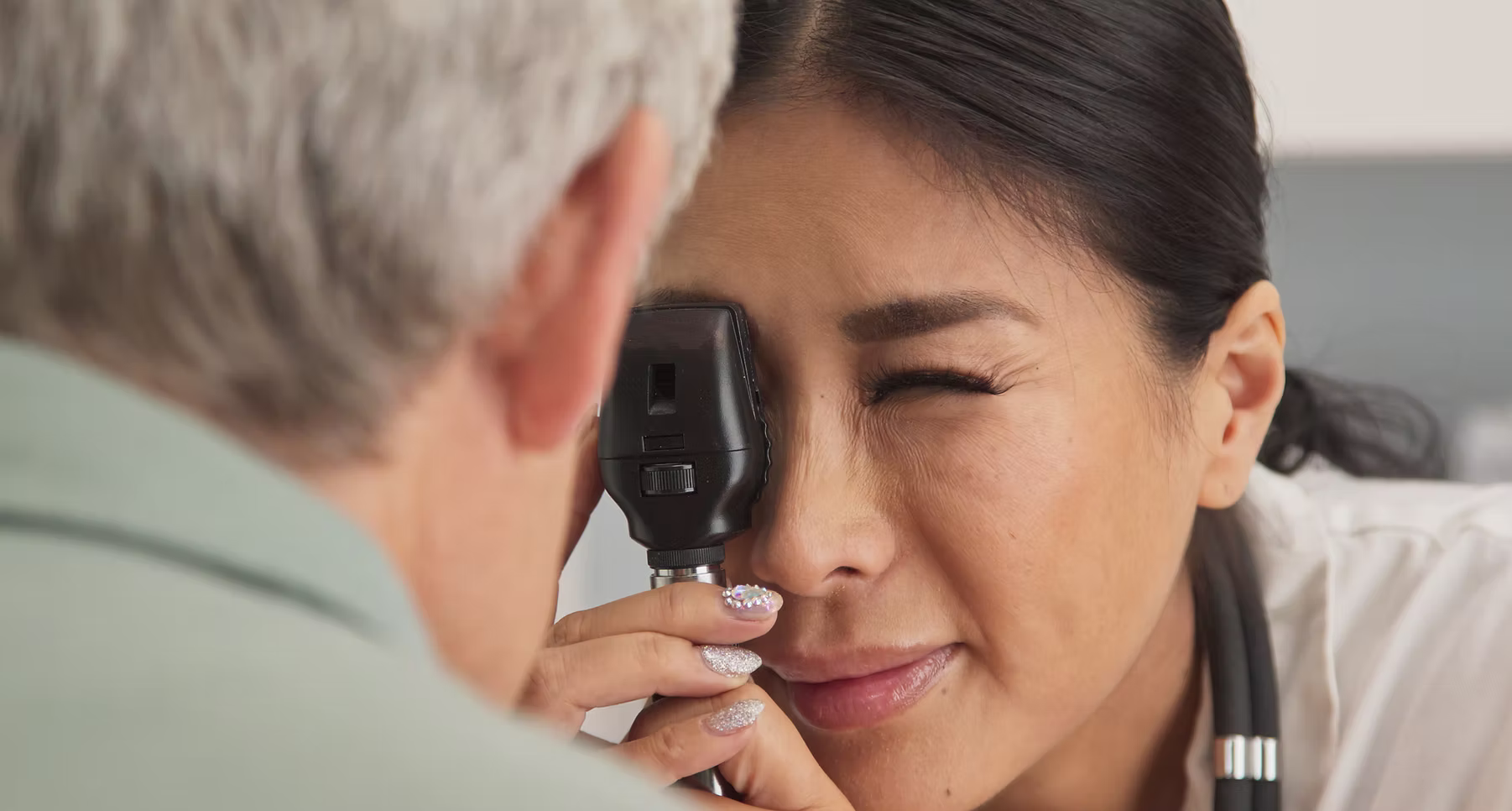 Healthcare professional examining an older man's eye with an ophthalmoscope during an eye checkup.