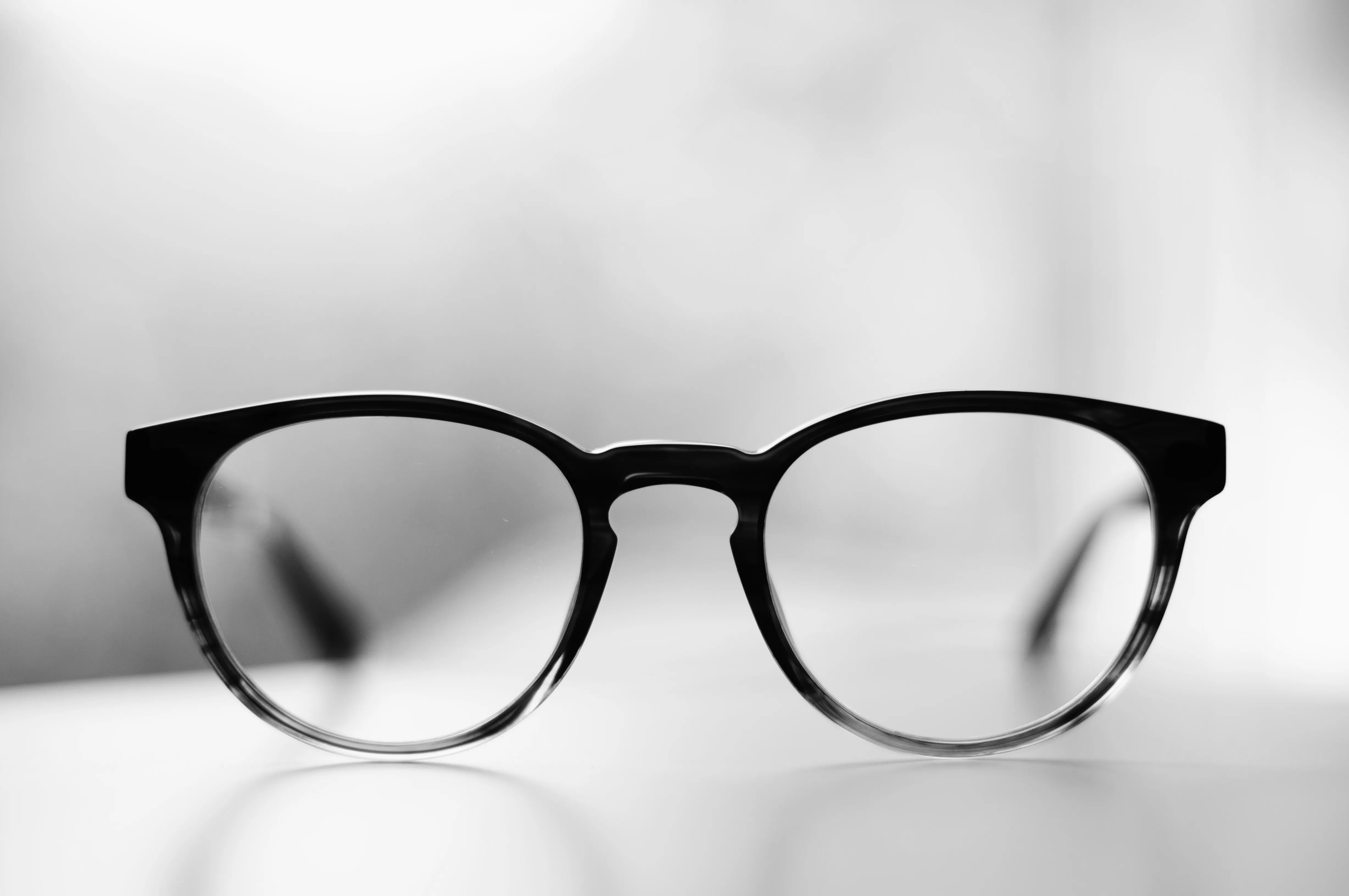Black-framed eyeglasses with clear lenses on a white surface with a blurred background.