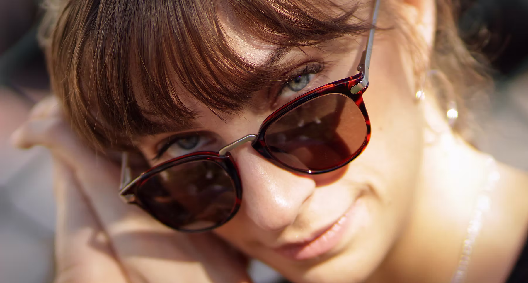 Close-up of a woman wearing sunglasses with light brown hair and blue eyes, smiling slightly.