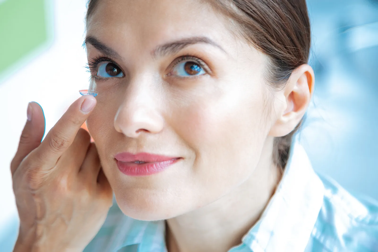 Smiling woman about to insert a contact lens into her eye