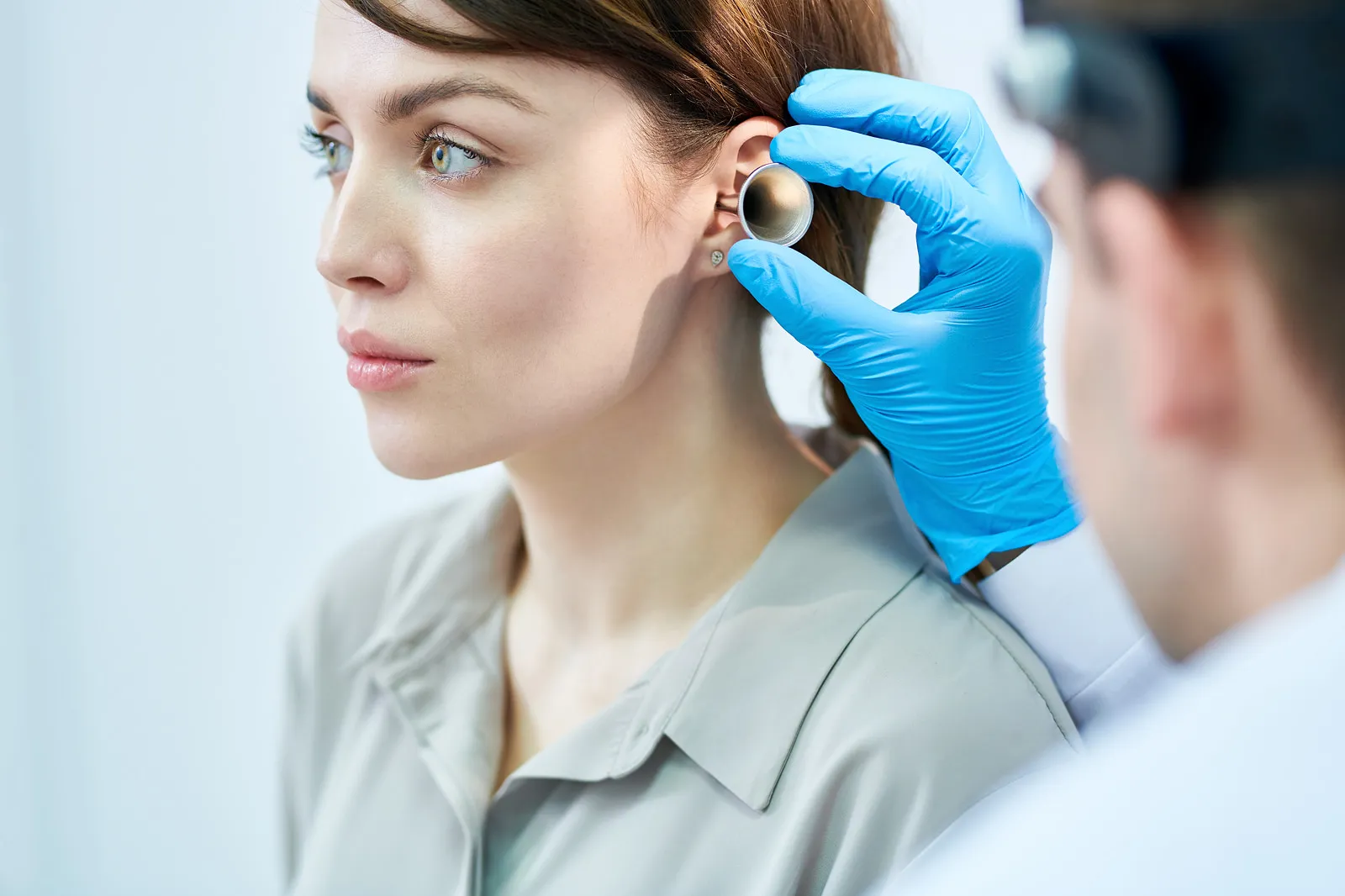 Audiologist in blue gloves examining a woman's ear with an otoscope during a hearing test