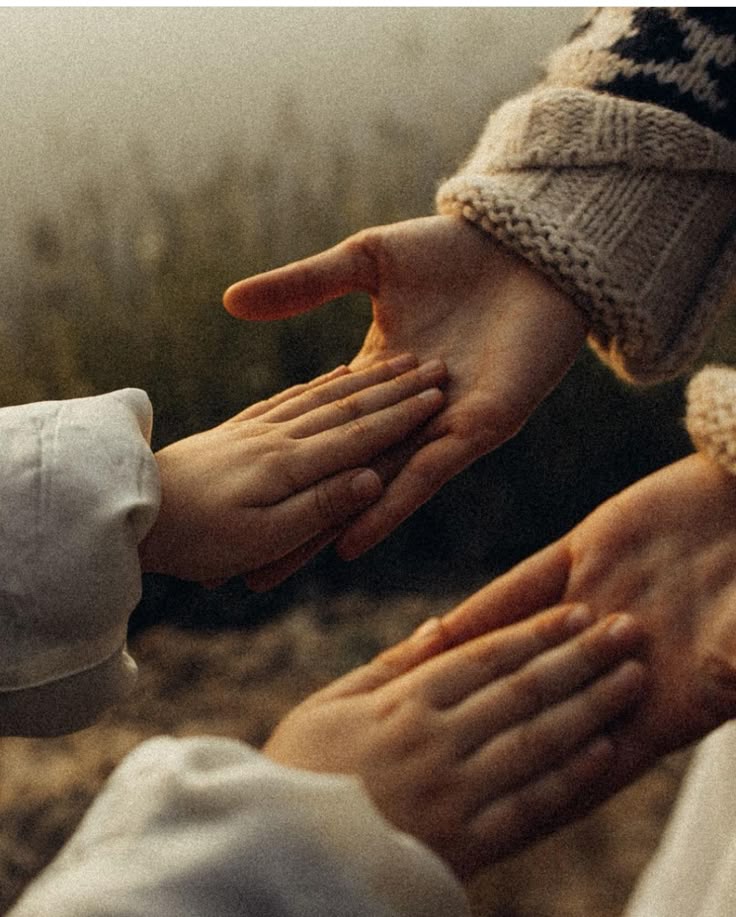 Close-up of two adult hands touching smaller hands of children outdoors.