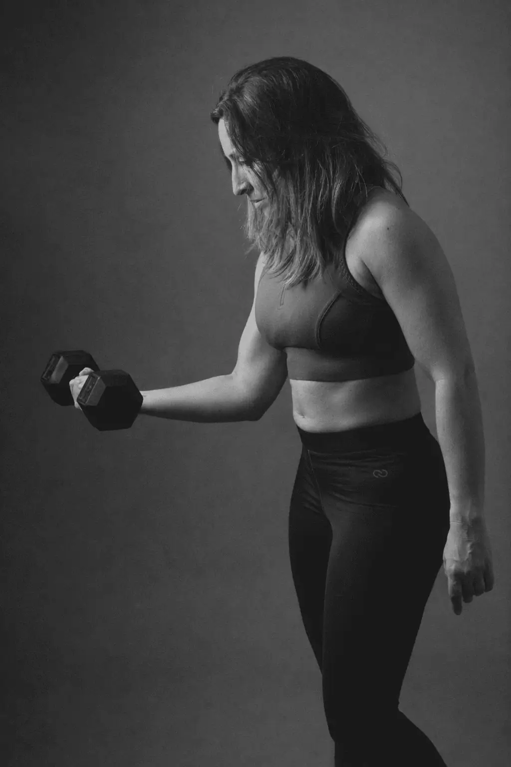 Rear view of a woman in athletic wear standing with hands on hips against a cloudy sky.