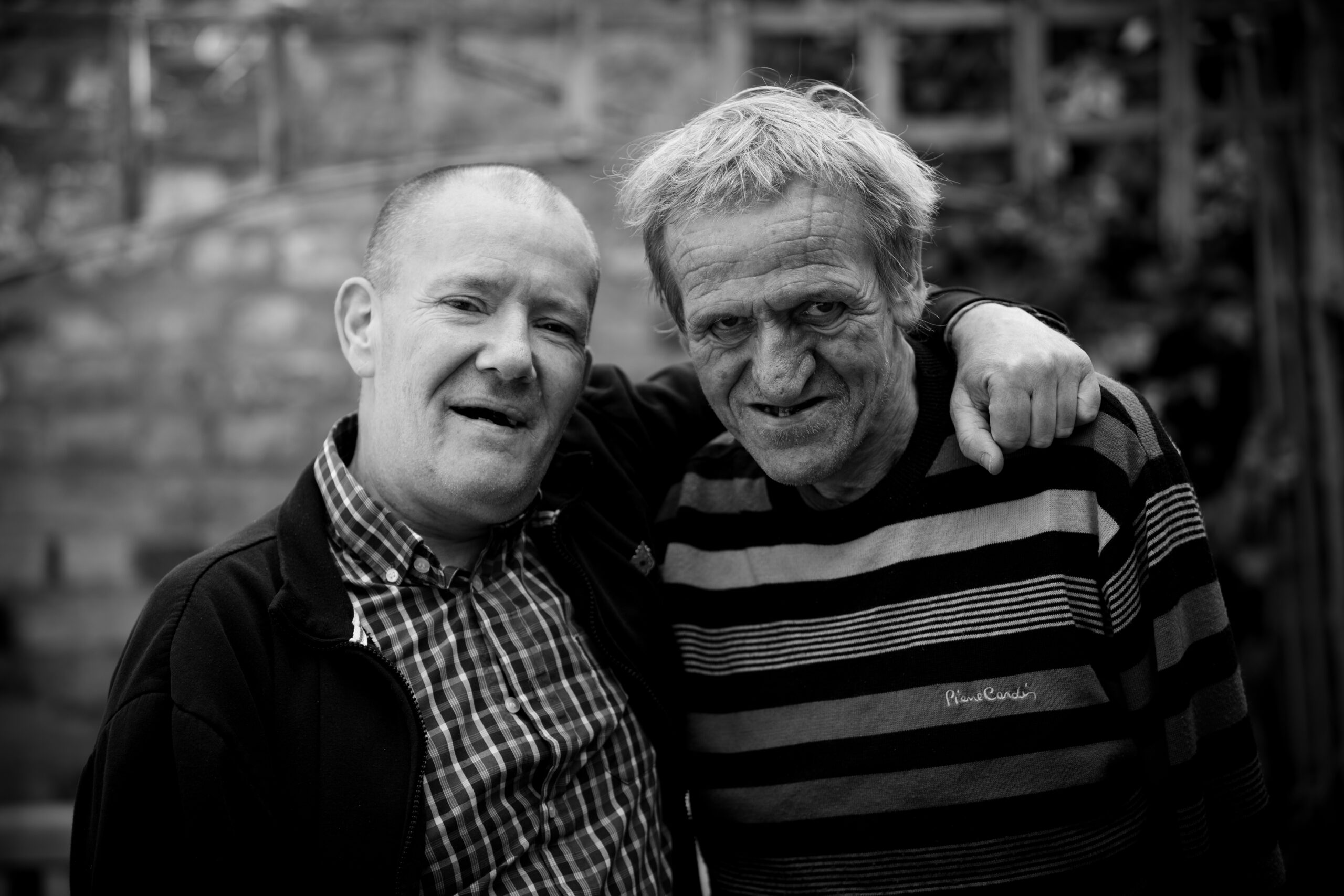 Black and white photo of two middle-aged men, one with his arm around the other, smiling at the camera.