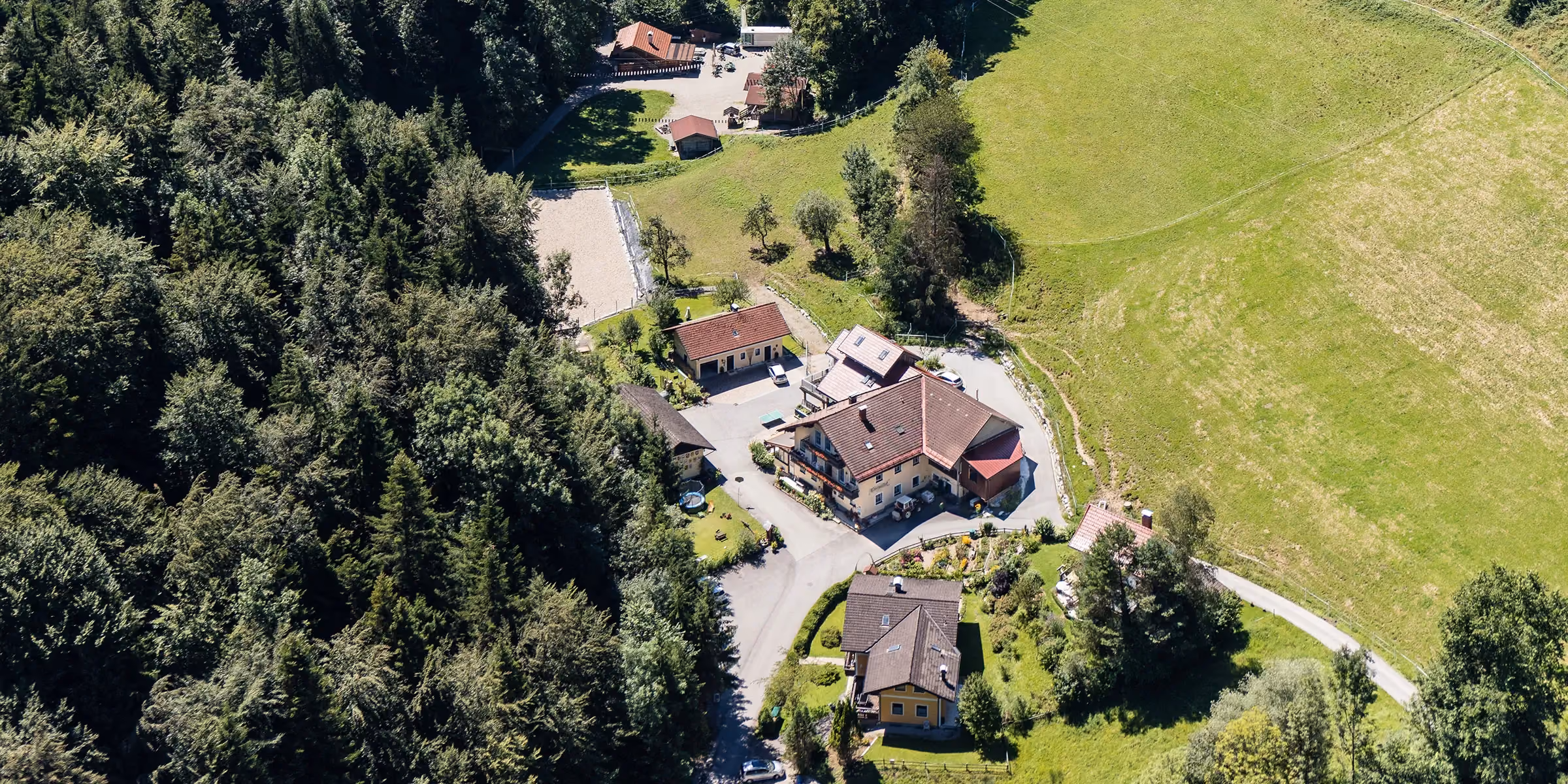 Luftaufnahme des Tobelmühlhofs in Seeham mit Wald und Wiesen
