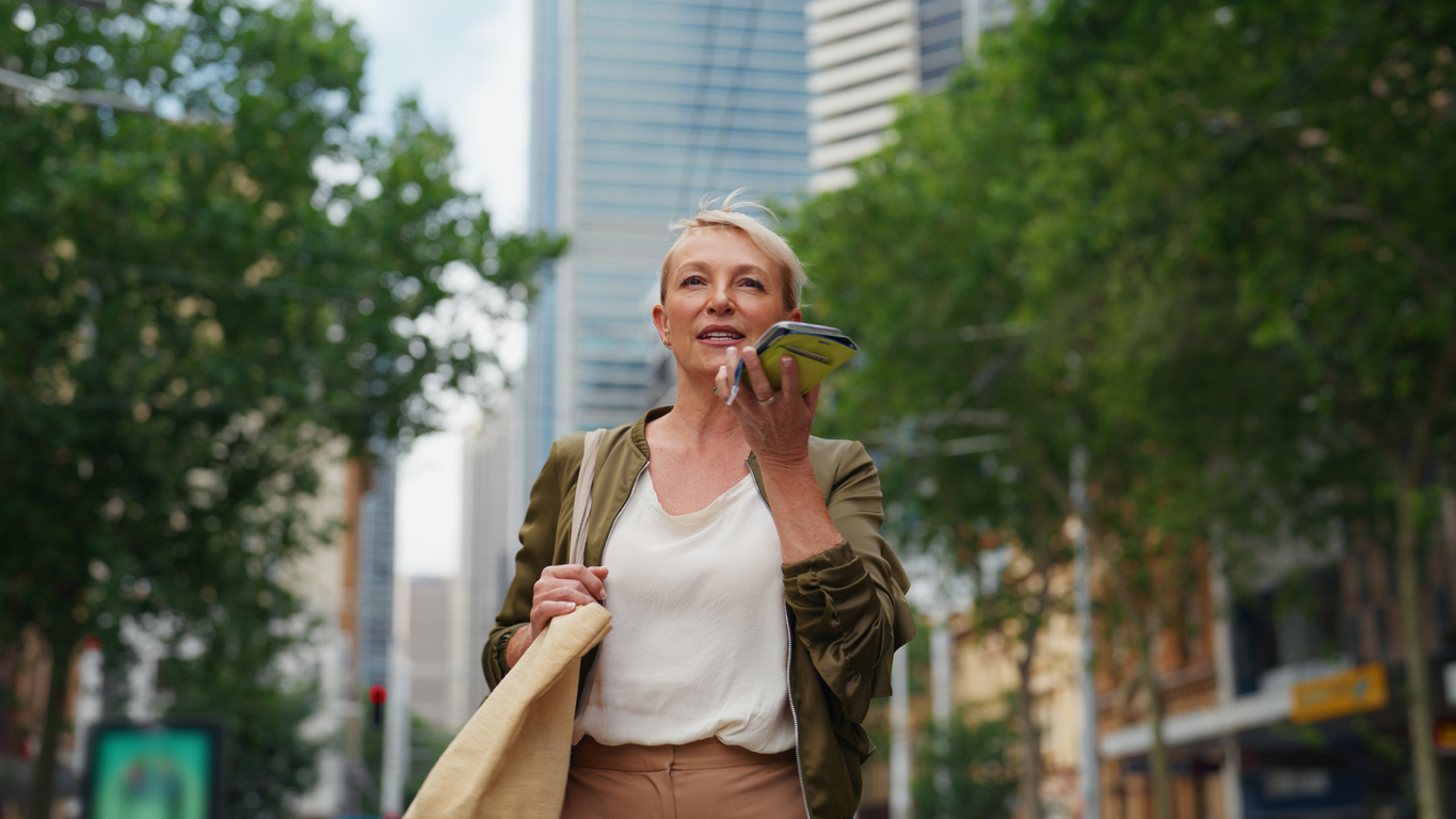 Una mujer de negocios utiliza un chatbot con IA en su smartphone mientras camina por una ciudad estadounidense, lo que muestra la adopción de agentes de IA en la tecnología empresarial.