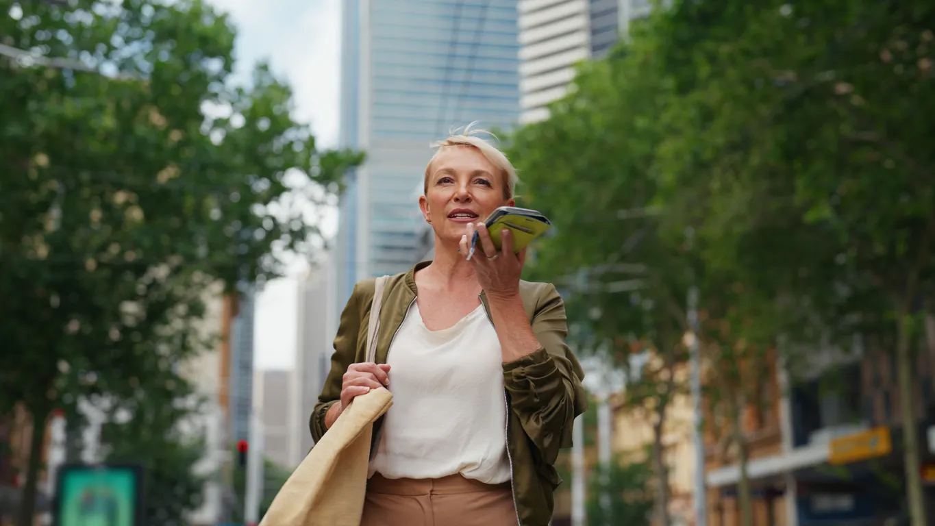 Una mujer de negocios utiliza un chatbot con IA en su smartphone mientras camina por una ciudad estadounidense, lo que muestra la adopción de agentes de IA en la tecnología empresarial.